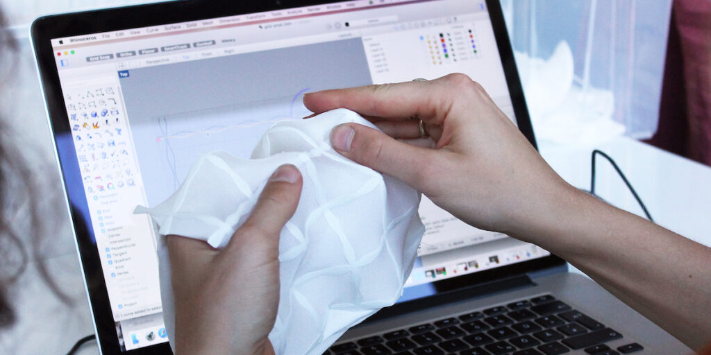 self shaping textiles are held towards the camera by two hands